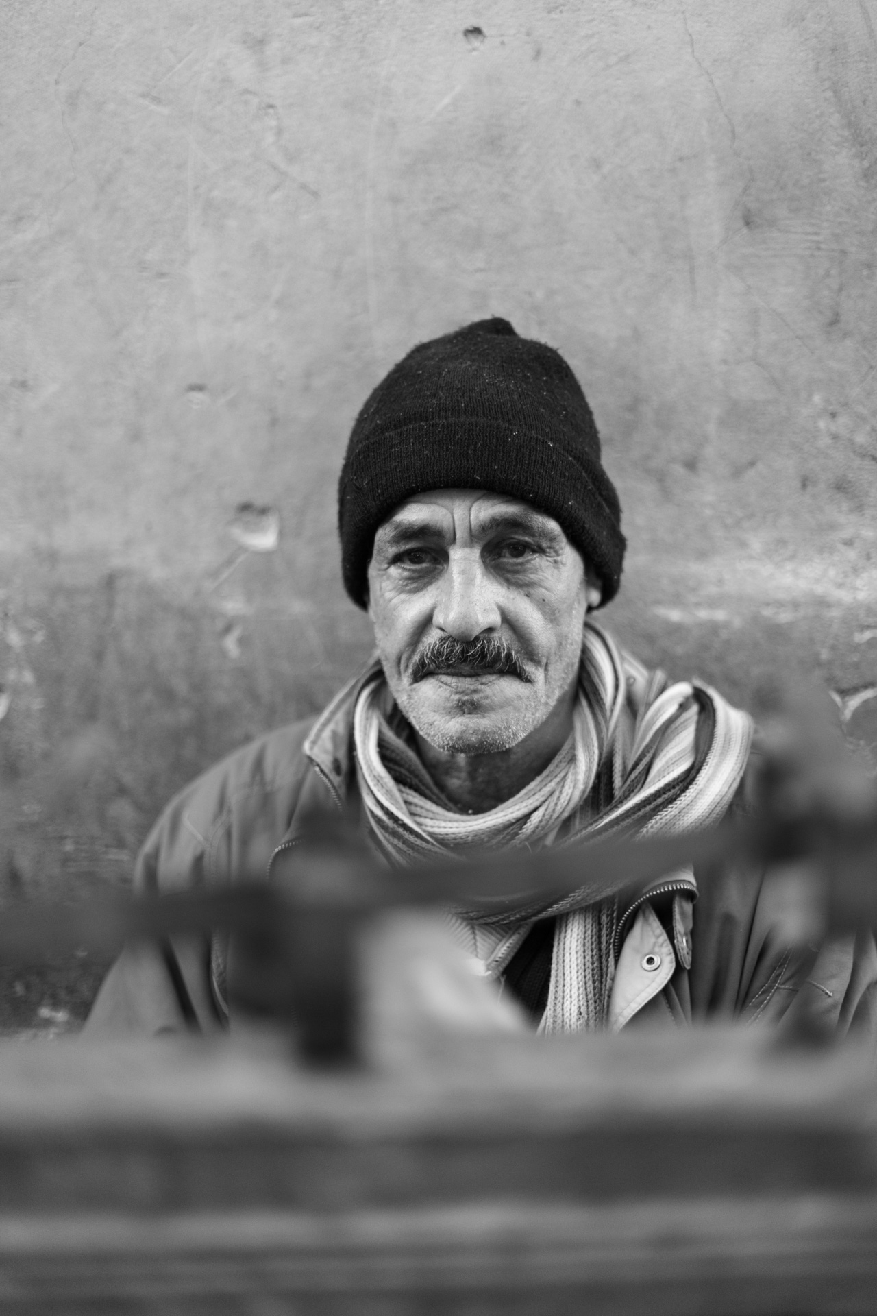 Direkter Blick eines Mannes mit schwarzer Mütze und gestreiftem Schal vor verwitterter Wand, dokumentarisches Porträt aus Marrakesch von Nietze